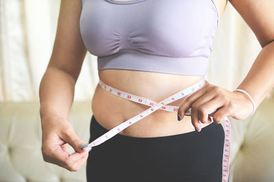 Midsection of woman measuring abdomen