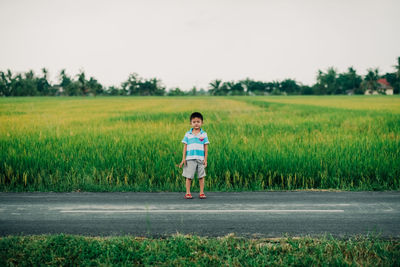 Full length of boy standing on road against field