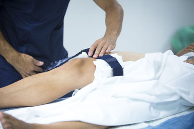 Midsection of doctor examining patient leg on hospital bed