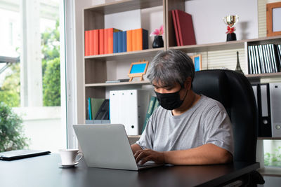 Rear view of man using mobile phone at home