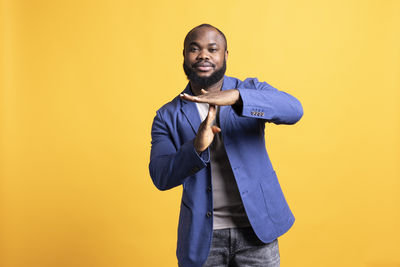 Portrait of young man standing against yellow background