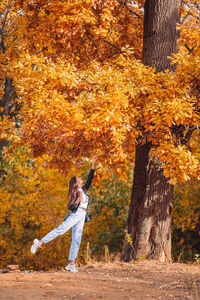 Full length of young woman touching autumn leaf at forest