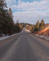 Empty road by trees against sky in city