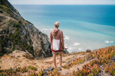 Rear view of woman standing on mountain against sea