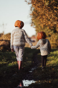 Rear view of young girls holding hands with pumpkins for heads.