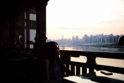 Portrait of woman sitting in city against sky during sunset