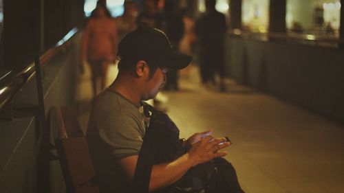 Side view of man using mobile phone while sitting on bench at night