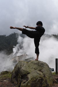 Young man practicing karate on rock formation in foggy weather