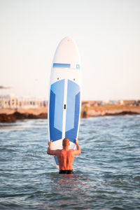 Rear view of shirtless male surfer with surfboard in sea