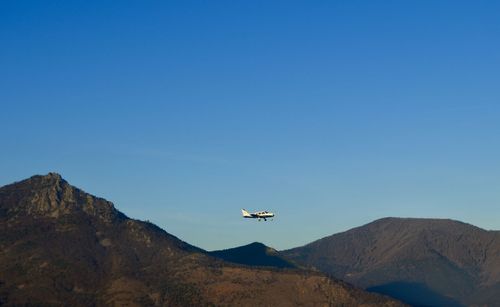 Low angle view of airplane flying over mountains against clear blue sky