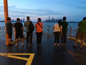 Rear view of people standing on shore against sky