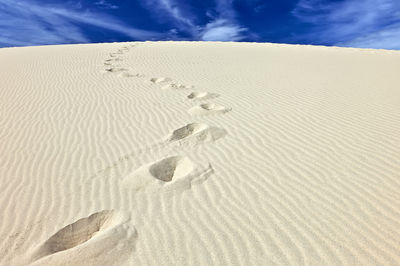 Footprints on sand in desert against sky