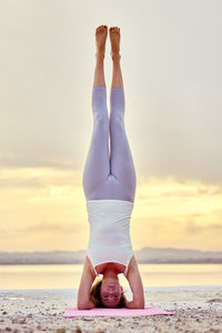 Full length of woman doing handstand at beach during sunrise