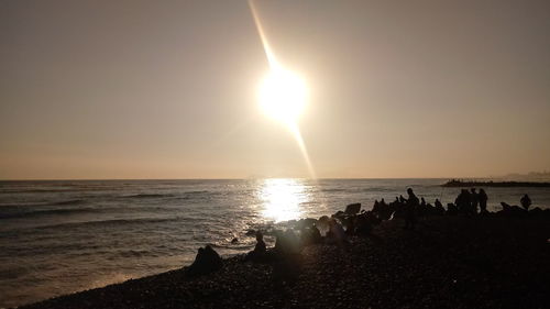 Silhouette people on beach against sky during sunset
