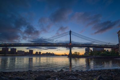 Suspension bridge over river against cloudy sky