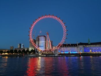 Illuminated ferris wheel by river against sky in city - london eye