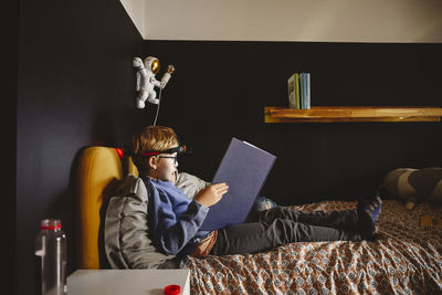 Boy with brother reading book on bed at home