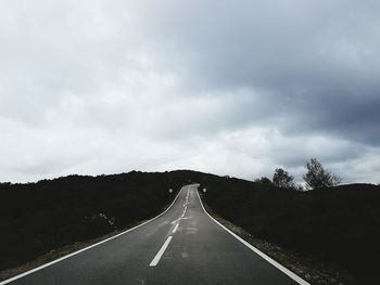 Empty road along trees and against sky