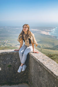 Portrait of young woman standing on retaining wall