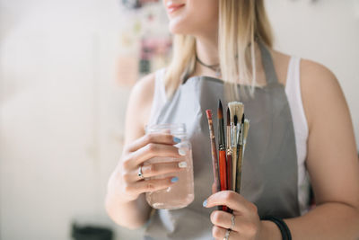 Midsection of artist holding jar and paint brushes at workshop