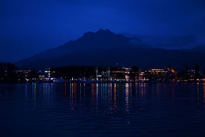 Illuminated city by lake against sky at night