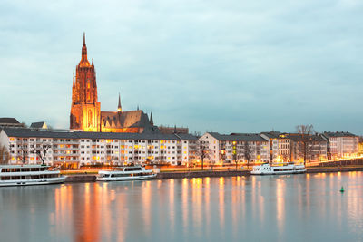 Illuminated buildings by canal against sky in city