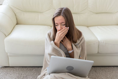 Young woman using phone while sitting on sofa at home