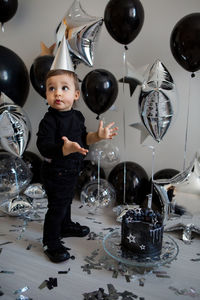 Boy stands next to a festive black cake and balloons