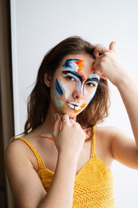 Close-up portrait of young woman with face paint against wall at home