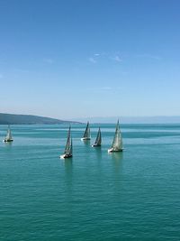Sailboats sailing in sea against blue sky