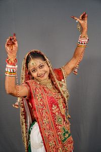 Portrait of smiling young woman with arms raised against gray background