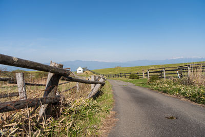 Road amidst field against clear blue sky