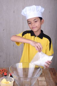 Boy wearing chef hat preparing food in kitchen at home