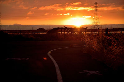 Road by silhouette trees against orange sky during sunset