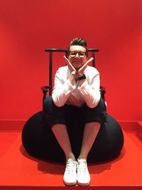 Portrait of young man sitting against red wall