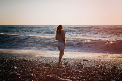 Rear view of woman standing on beach against clear sky