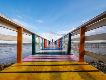 Empty walkway leading towards sea against sky