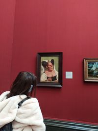 Rear view of woman photographing against red wall