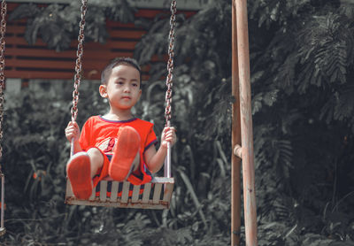 Portrait of boy sitting on swing at playground