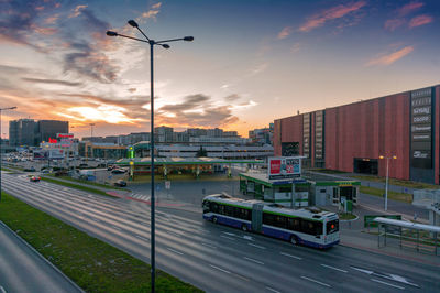 Cars on street by buildings against sky during sunset