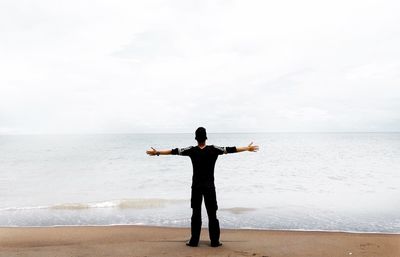 Rear view of man standing on shore at beach against sky