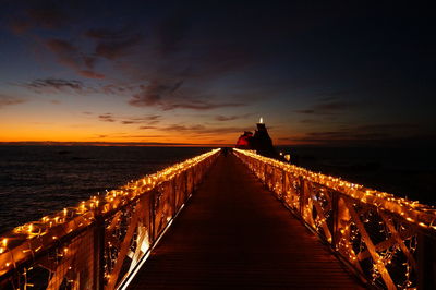 Illuminated bridge over sea against sky during sunset