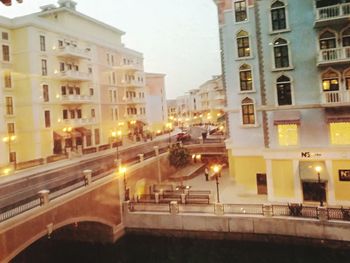 Illuminated buildings by street in city against sky