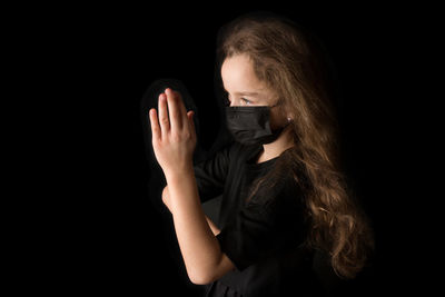 Portrait of woman holding covering face against black background