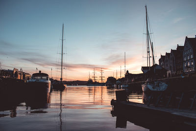 Sailboats moored at harbor against sky during sunset