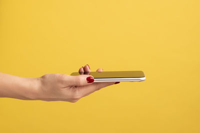 Cropped hand of woman holding smart phone against colored background
