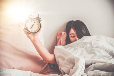 Sleepy woman holding alarm clock on bed