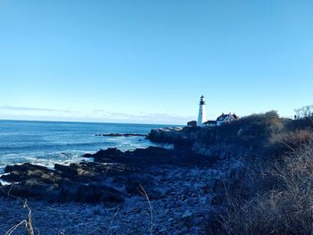 Lighthouse by sea against clear blue sky