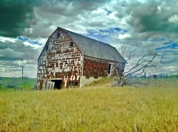 Barn on grassy field against cloudy sky