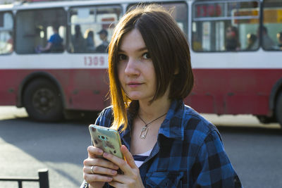 Portrait of woman using phone on road against bus